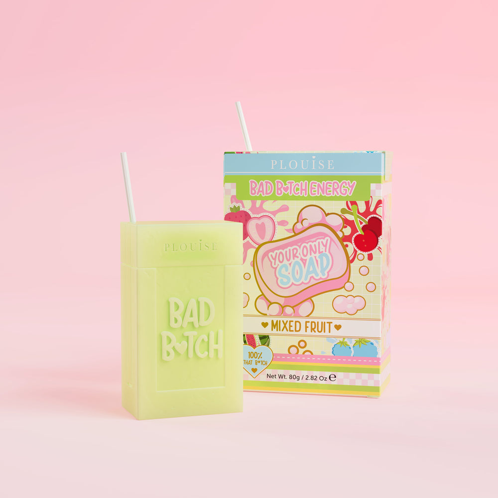 Een groen stuk zeep met 'Bad Bitch' erop gegraveerd, vergezeld van een kleurrijke sapdoos met het label 'Mixed Fruit' erop, gepresenteerd op een roze achtergrond.