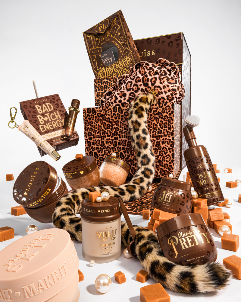 Ein luxuriöses Beauty-Geschenkset mit braunen und Leopardenmuster-Elementen, einschließlich einer Geschenktüte mit Leopardenmuster, einem Schwanz mit Leopardenmuster und mehreren Kosmetikbehältern in Braun- und Beigetönen, angeordnet auf einem weißen Hintergrund mit karamellfarbenen Würfeln und Perlen.