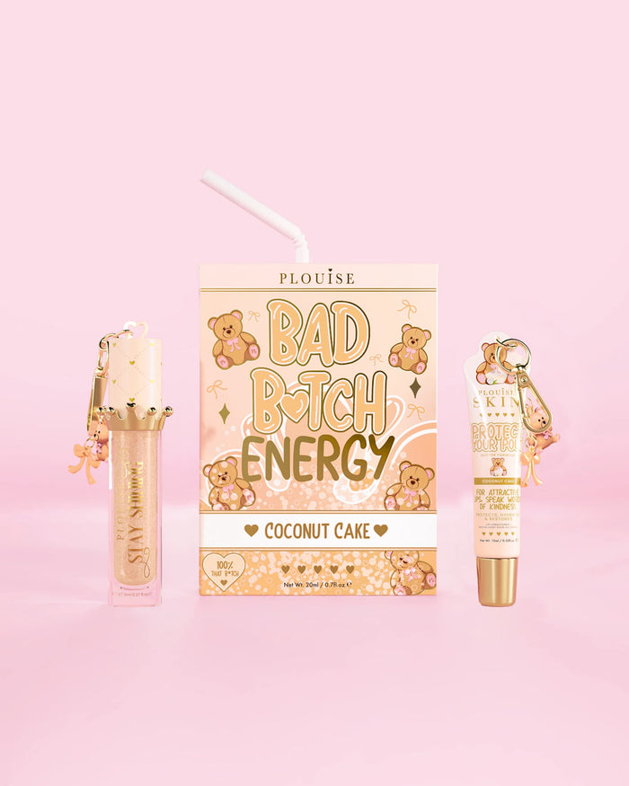 A P.Louise Teddy Glitter Bad Bitch Energy Lip Duo in coconut cake scent featuring a lip conditioner and lip oil against a pink background