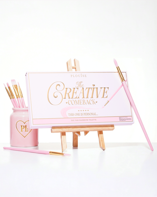 A closed pink P.Louise Creative Comeback XXXL Rainbow Eyeshadow Palette placed on an art easel surrounded by makeup brushes