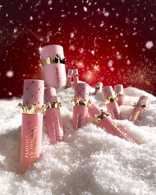 Giant Crown Stay Shining Lip OIl gift box surrounded by pink lip oils in snow on a red background