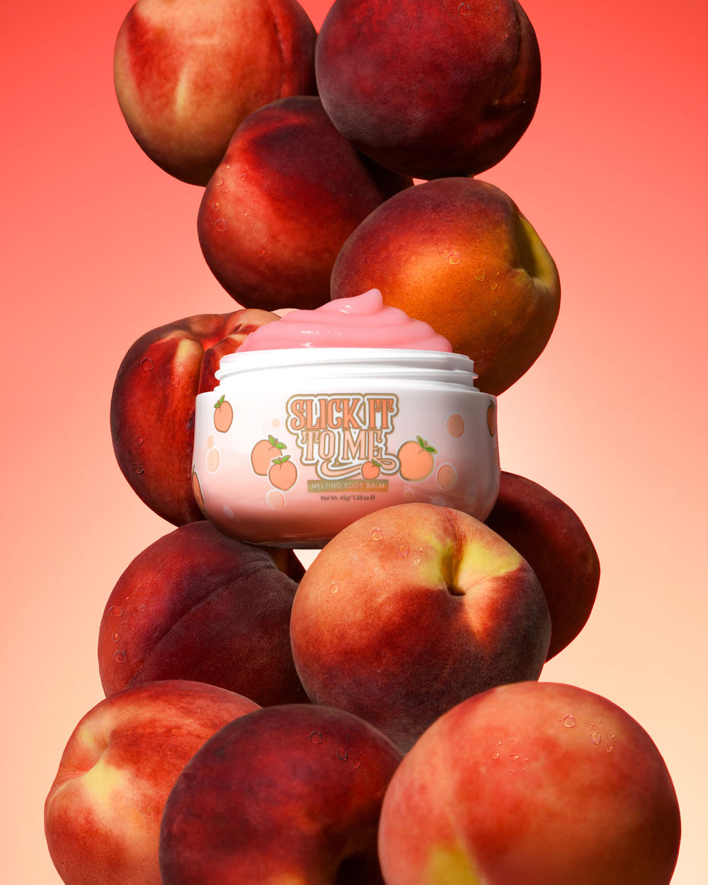 Krukke med P. Louise Slick It To Me Peach Melting Body Balm med rosa krem omgitt av fersken på en gradient bakgrunn