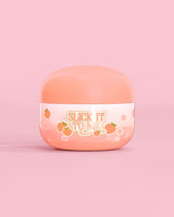 Krukke med P. Louise Slick It To Me Peach Melting Body Balm med rosa bakgrunn