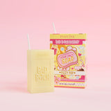 Een geel stuk zeep met 'Bad Bitch' erop gegraveerd, vergezeld van een kleurrijke sapdoos met het label 'Fizzy Pop' erop, gepresenteerd op een roze achtergrond.
