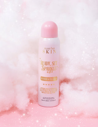 An aerosol can of P. Louise Ready Set Sparkle Glitter Setting Spray in To Have And To Gold gold shimmer against a light pink background with clouds and sparkles