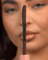 Gros plan d'une baguette de mascara imperméable P.Louise Tearproof tenue devant un visage flou